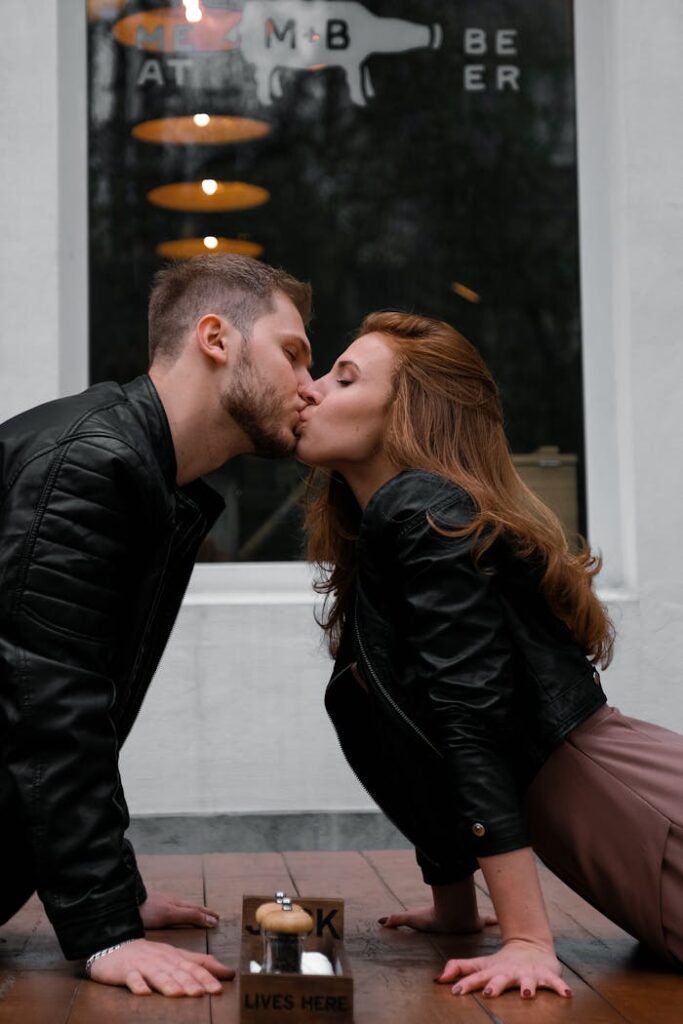 A couple shares a passionate kiss on a sidewalk outside a cafe.